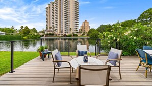 Una terraza con mobiliario exterior, vistas a un lago y un edificio alto al fondo.