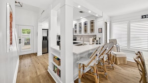 Una cocina moderna con armarios blancos, una isla central con taburetes y una zona de comedor con mesa y sillas blancas.