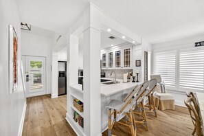 Une cuisine moderne avec des meubles blancs, un îlot central doté de tabourets de bar et un coin repas avec une table et des chaises blanches.