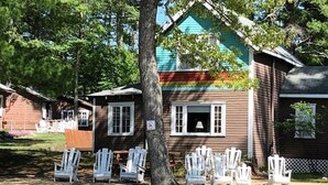 Een rij witte Adirondack-stoelen voor een houten gebouw met een blauw dak.
