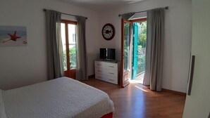 A bedroom with a bed, a dresser, a TV, and a window with curtains.