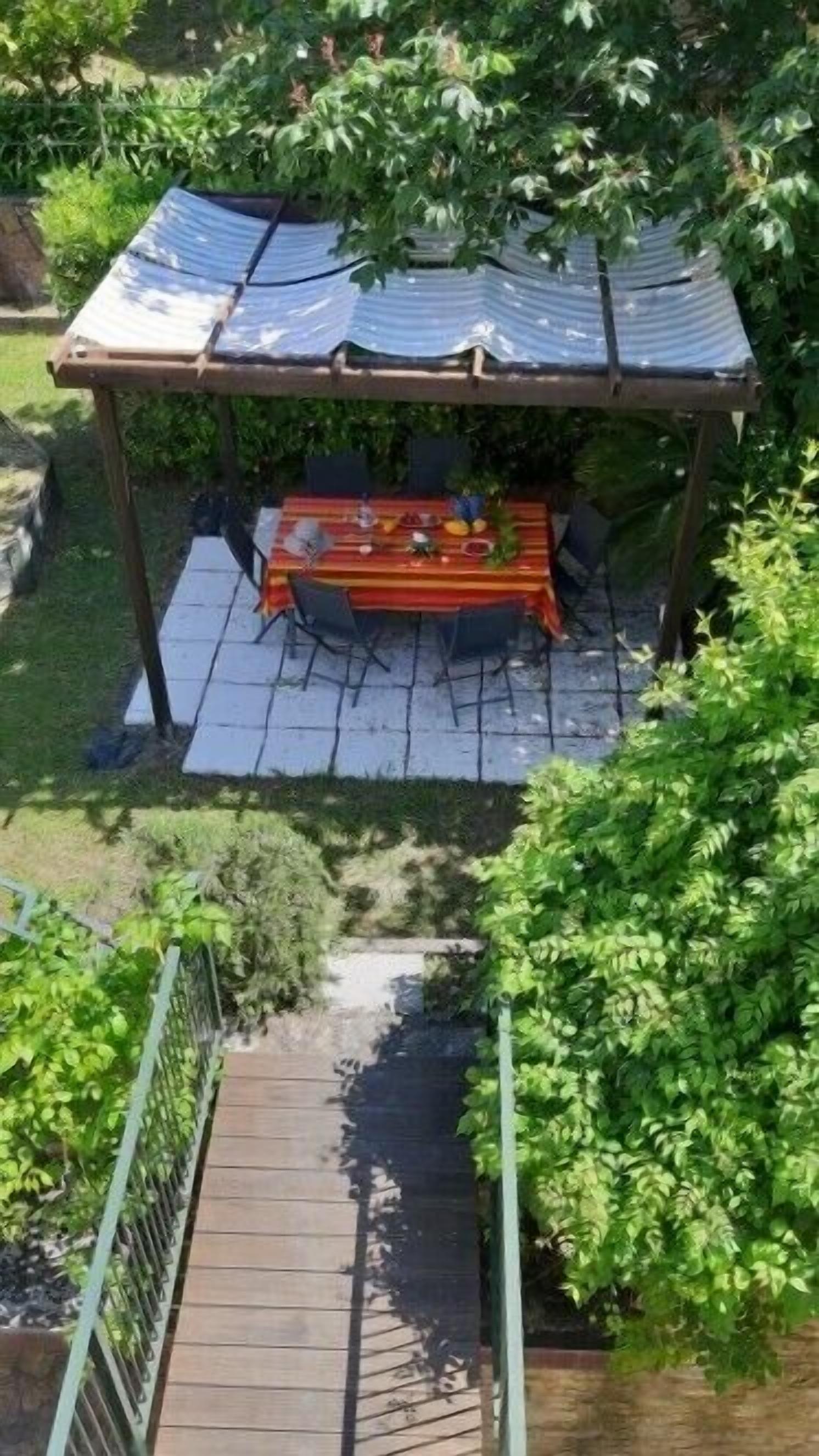 Un espace extérieur abrité, aménagé pour prendre les repas, avec une table et des chaises, le tout entouré de verdure.