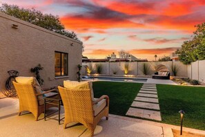 Un patio con mobiliario de mimbre, una piscina y un césped bien cuidado.