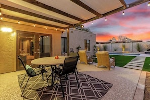 An outdoor patio with a round table and chairs, a covered seating area, and a view of a sunset.