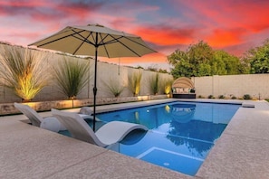 A swimming pool with lounge chairs, an umbrella, and decorative plants.