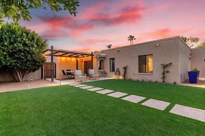 A modern house with a well-maintained lawn, outdoor seating, and a clear view of the sky.