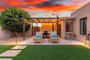Eine Garten-Terrasse mit einer Pergola, zwei Korbstühle mit Kissen, einem Tisch und einem Fahrrad.