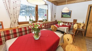 A cozy dining area with wooden furniture, a red tablecloth, and a vase of tulips. - Schneiderbauer (Waidring)