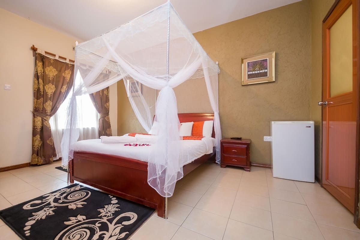 A bedroom with a four-poster bed, a bedside table, a nightstand, a refrigerator, and a door.