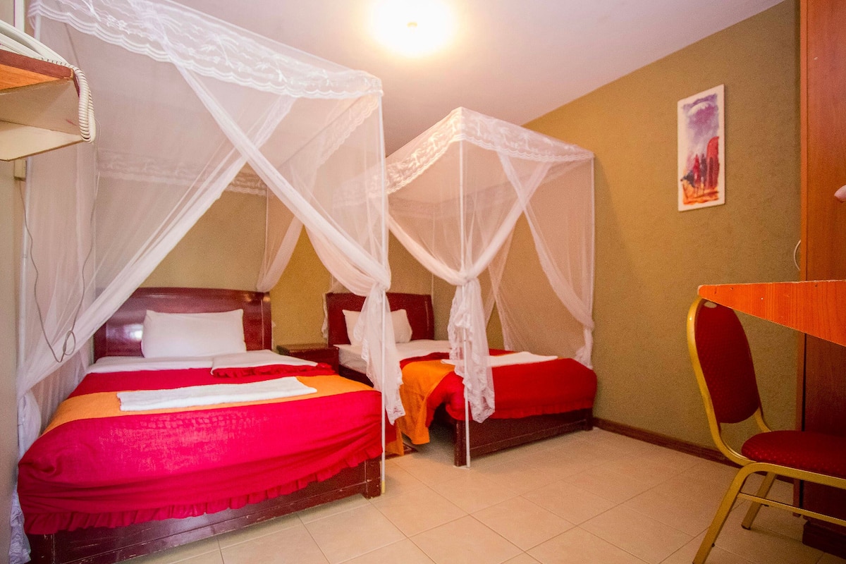 A room with two beds, each with a canopy, a wooden chair, and a small table.