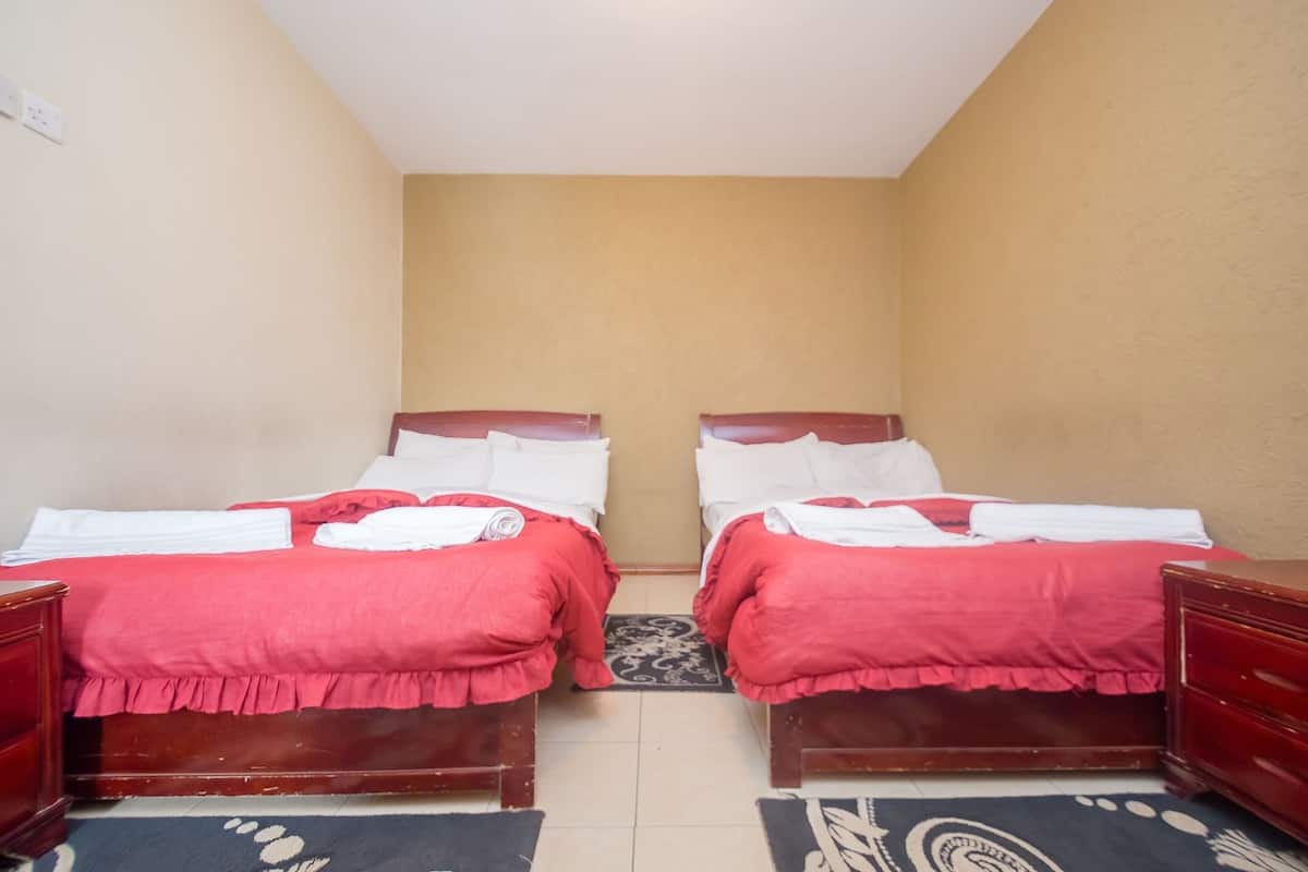 A room with two beds, each with a red bedspread and white pillows, wooden headboards, and a small rug on the floor.