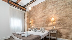 A bedroom with a wooden floor, a bed with white linens, two bedside lamps, and a brick wall. - MY LOFT 4 YOU RUZAFA STYLE II (Valencia)