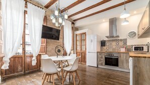 A rustic kitchen with wooden beams, a dining table with chairs, a TV, and a microwave. - MY LOFT 4 YOU RUZAFA STYLE II (Valencia)