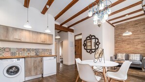 A modern kitchen with wooden beams, a washing machine, and a dining area with white chairs and a table. - MY LOFT 4 YOU RUZAFA STYLE II (Valencia)