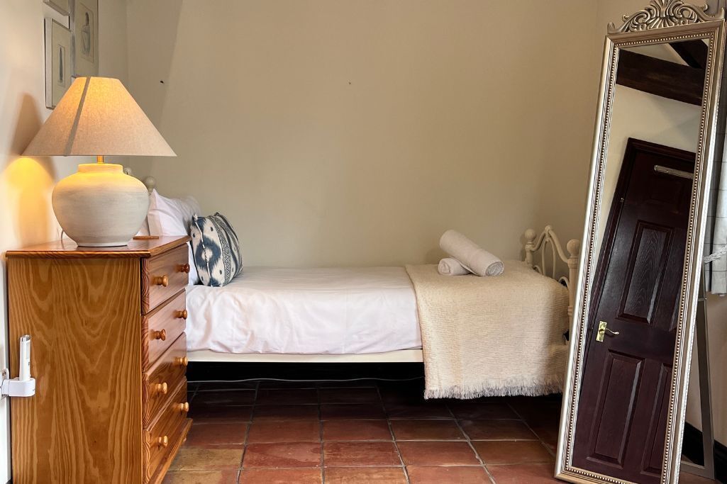 Ein Schlafzimmer mit einem Bett, einer hölzernen Kommode, einer Lampe, einem Spiegel und einer Tür.