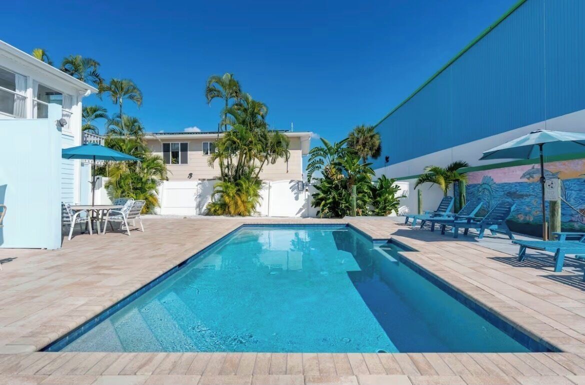 Une piscine rectangulaire, bordée d’une terrasse carrelée, entourée de chaises longues et de parasols.