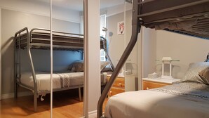 Habitación con literas, escritorio y silla, ventana con persianas y mesita de noche con lámpara.