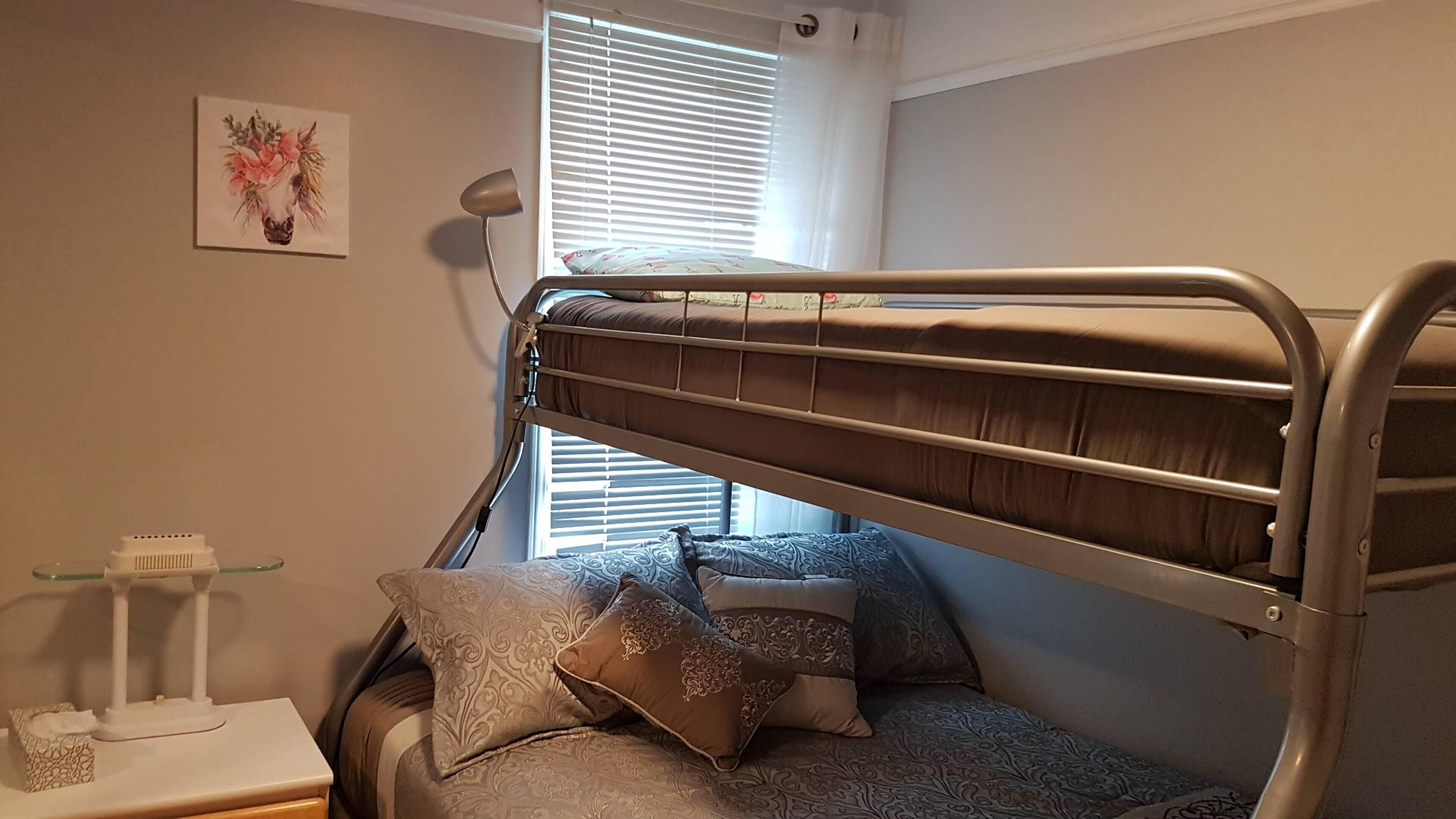 Ein Stockbett mit Kopfteil, ein Nachttisch mit Lampe und ein Fenster mit Jalousien.