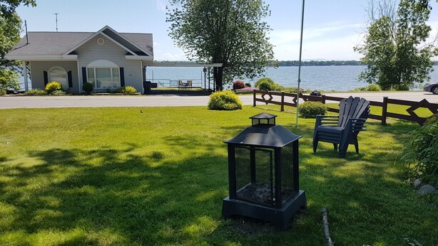 Una casa con un porche con vista a un lago, un césped con un farol y sillas Adirondack.