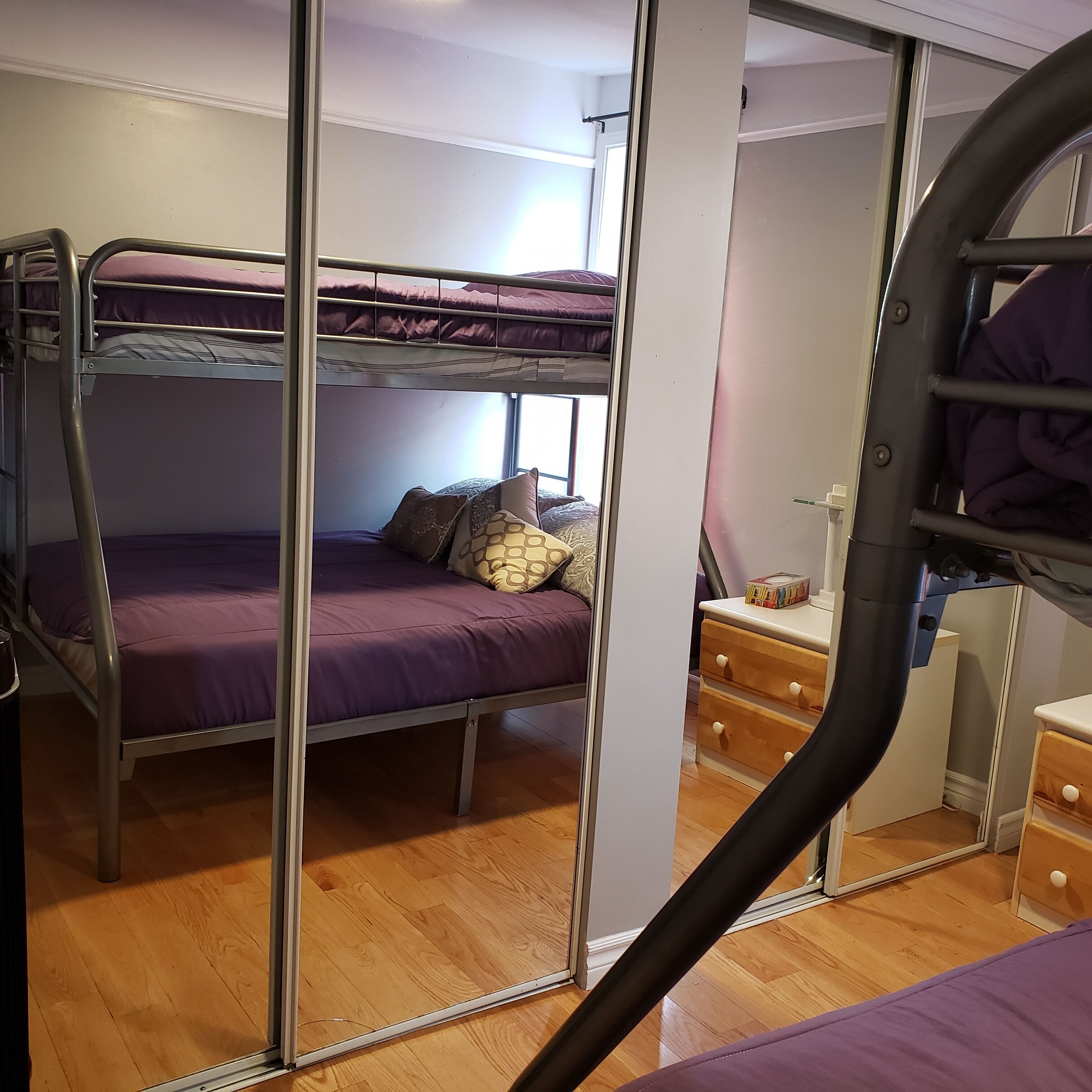 A bunk bed room with a wooden floor, a small wooden dresser, and a window.