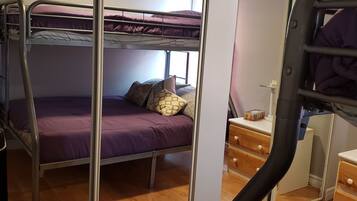 A bunk bed room with a wooden floor, a small wooden dresser, and a window.