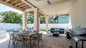 An outdoor patio with a dining table, chairs, a grill, and a pool. - New 4BR Oasis: Walk to Beach, Pool, Pet-Friendly! (Fort Myers Beach)