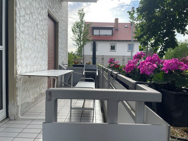 A balcony with a metal railing, a tiled floor, and potted plants with pink flowers. - 50 steps to river Main, Cycling, balcony into the greenery, ideal long stay (Mainstockheim)