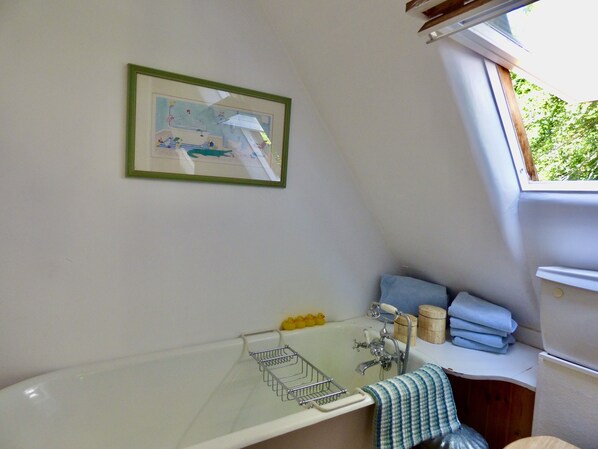 A bathroom with a bathtub, a window, a framed picture on the wall, and a towel rack.