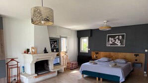 A bedroom with a fireplace, a bed with two pillows, a hanging light fixture, and a framed family photo on the wall. - Large Villa - Charming Provencal village - Swimming pool - Petanque court (PEYNIER)