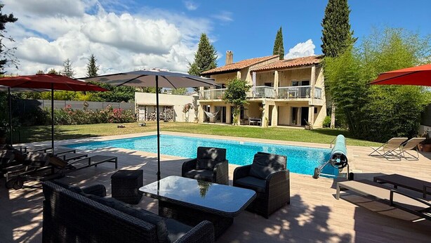 A poolside area with outdoor furniture, a clear blue pool, and a large house in the background. - Large Villa - Charming Provencal village - Swimming pool - Petanque court (PEYNIER)