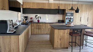 A modern kitchen with wooden cabinets, a central island, bar stools, and pendant lighting. - Large Villa - Charming Provencal village - Swimming pool - Petanque court (PEYNIER)