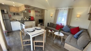A compact living space with a dining area, kitchenette, and a sofa with cushions. - Rent mobile home 6pers 40 m2 from 250 € per week (pont aven)