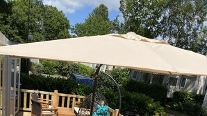 A wooden deck with a table set for four, surrounded by wicker chairs, and an umbrella providing shade. - Rent mobile home 6pers 40 m2 from 250 € per week (pont aven)