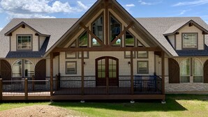 A two-story house with a prominent gable roof, large windows, and a covered porch with chairs.
