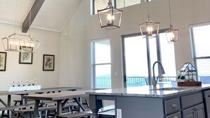 A spacious kitchen with a high ceiling, large windows, and modern pendant lighting.