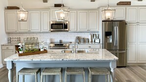 A modern kitchen with white cabinetry, stainless steel appliances, a granite countertop, and hanging pendant lights.
