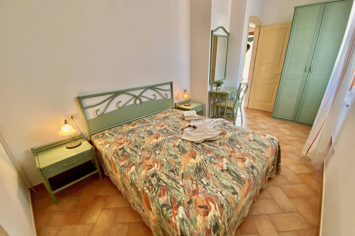 A bedroom with a bed, a nightstand, a lamp, a chair, and a wardrobe.