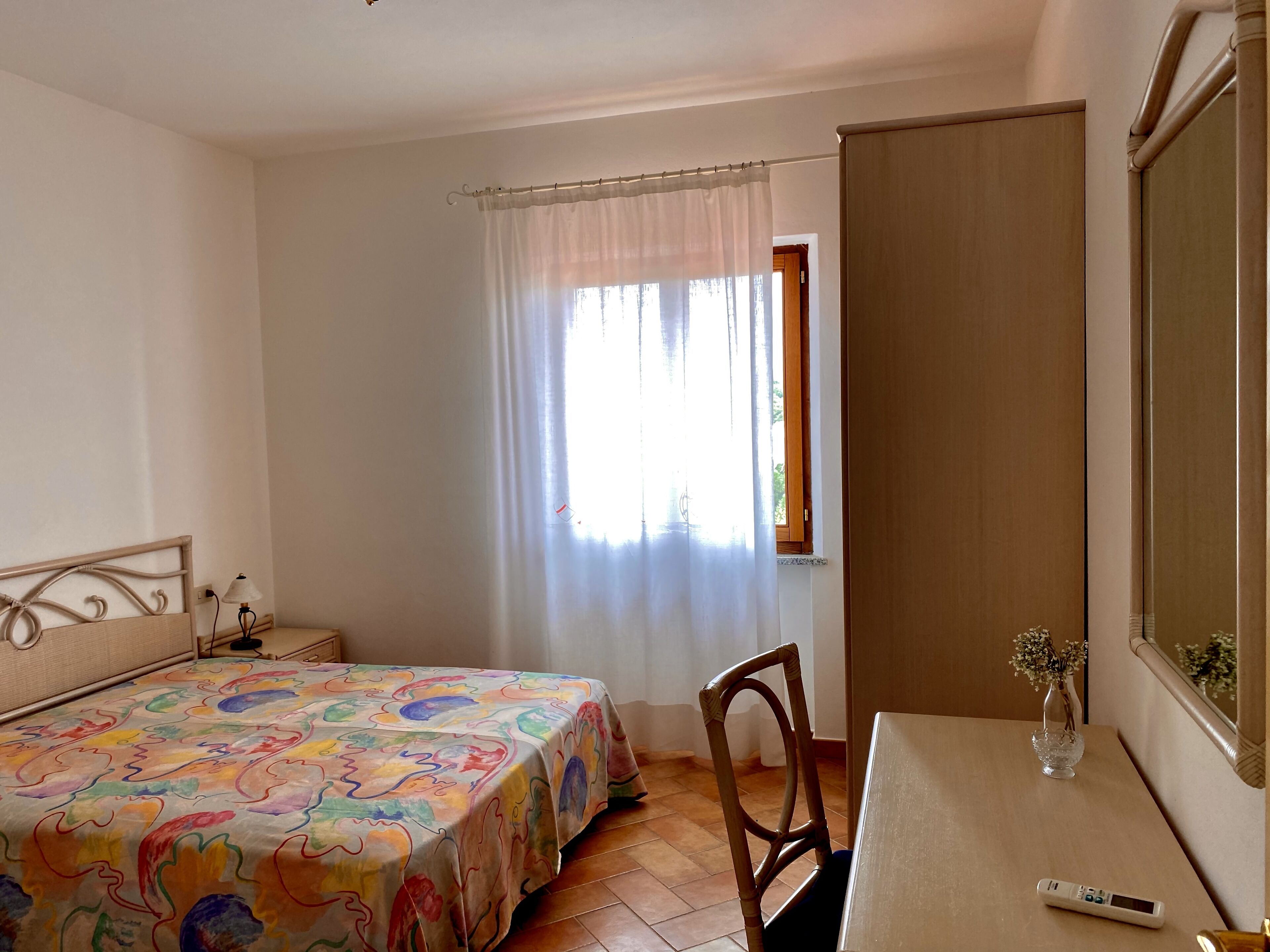 Ein Schlafzimmer mit Bett, Stuhl, Schreibtisch und einer Vase sowie einem Fenster mit Vorhängen.