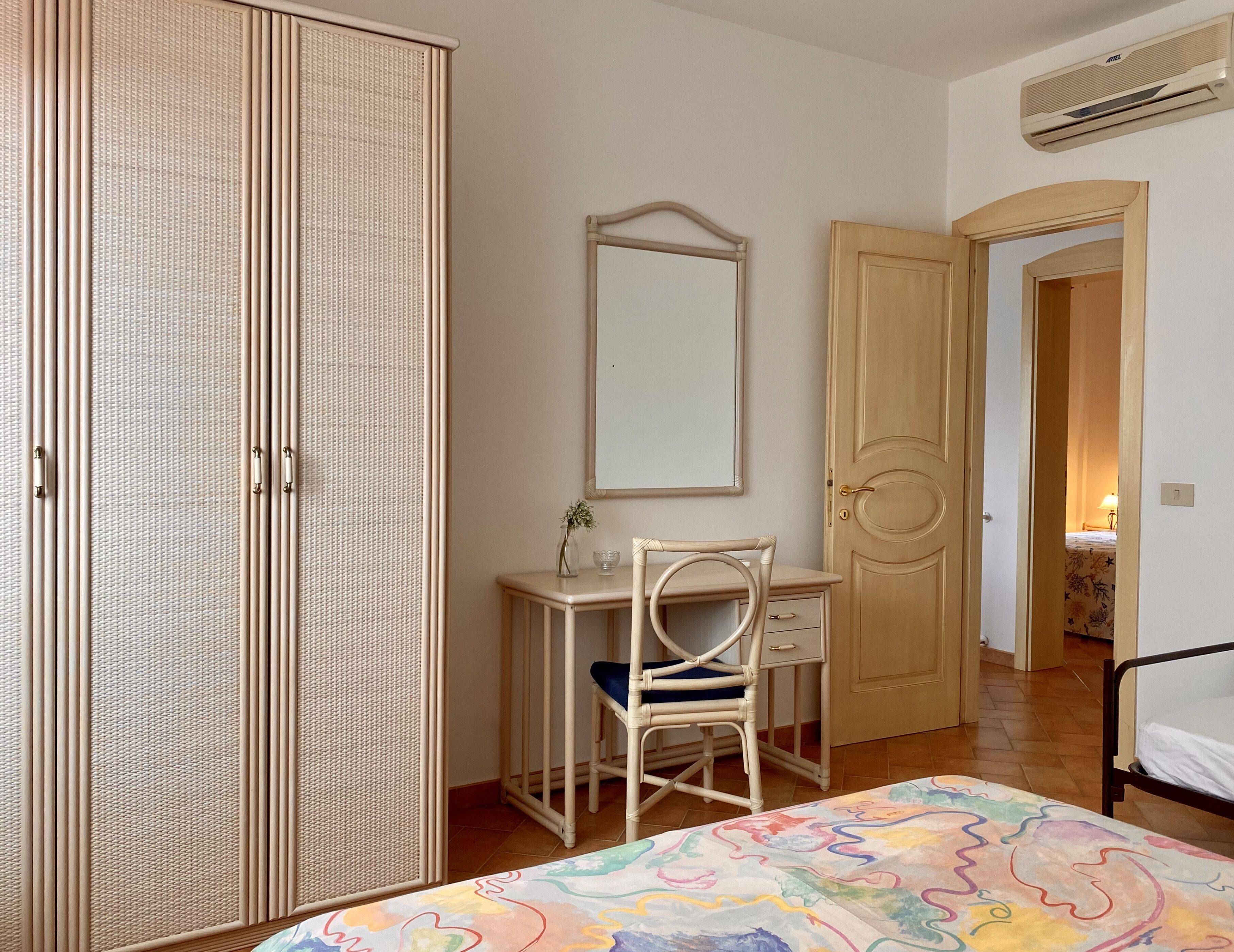 Une chambre à coucher comprenant un lit, un bureau avec une chaise, une armoire et une porte donnant sur une autre pièce.