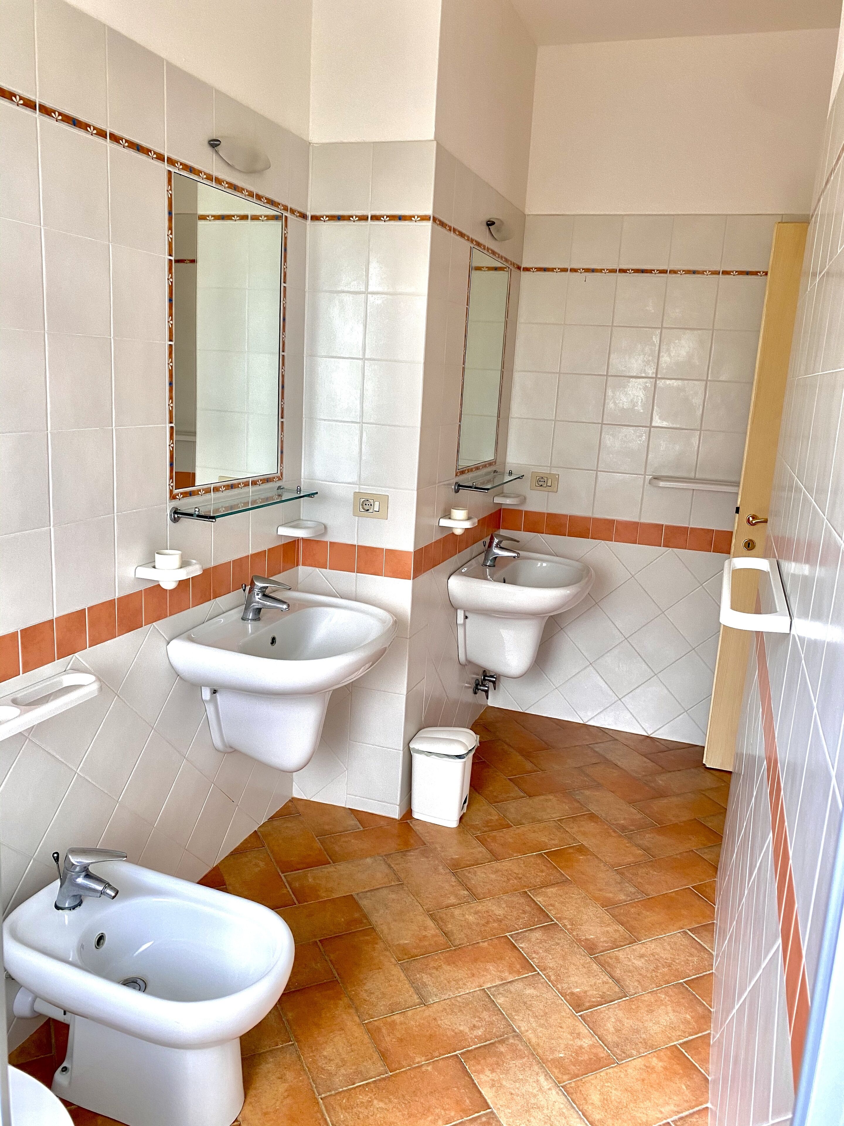 A bathroom with two sinks, a bidet, and a mirror.