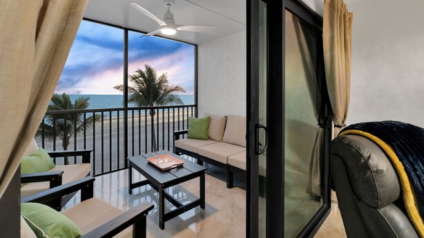 Een balkon met uitzicht op het strand, een bank, een tafel en een plafondventilator.
