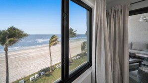 Een kamer met een groot raam met uitzicht op een strand, een bank en een bijzettafeltje.