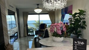 Een moderne hotelkamer met een marmeren vloer, een kroonluchter, een zithoek met uitzicht op zee, en een bordje met de WiFi-wachtwoord.