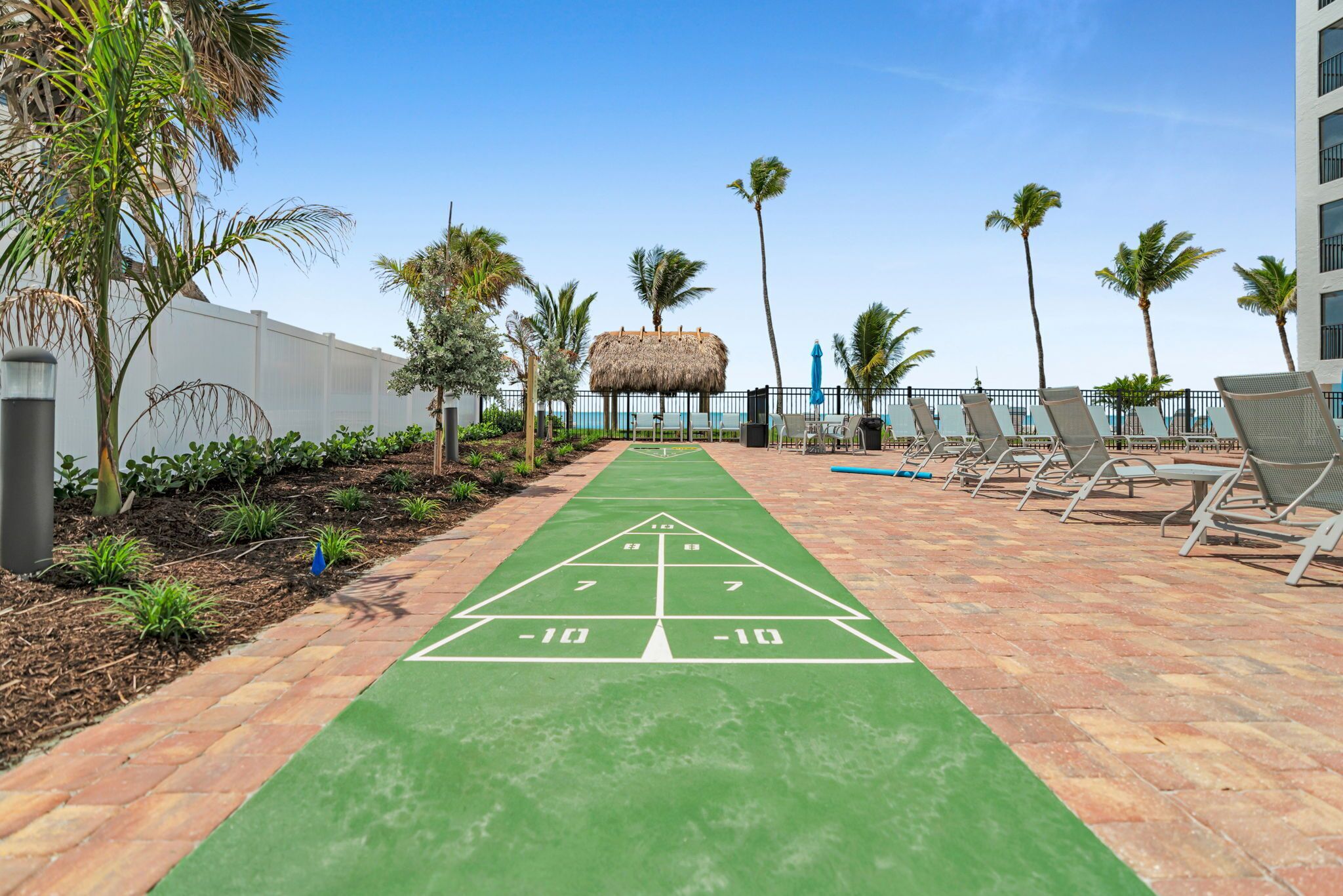 Een jeu de boules baan met een overkapping met rieten dak, omgeven door palmbomen en lounge stoelen.
