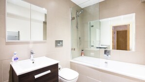 Een moderne badkamer met een wit wastafelmeubel, toilet, douche met glazen wanden en een grote spiegel.