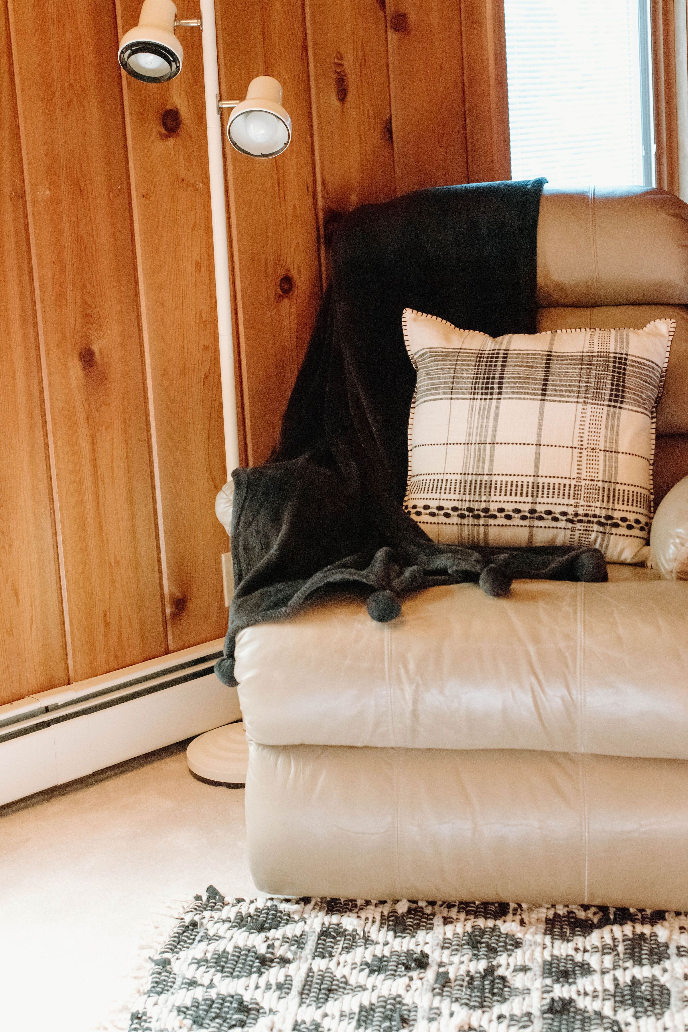 A cozy room with a leather sofa, a plaid pillow, a black throw blanket, and a woven rug.