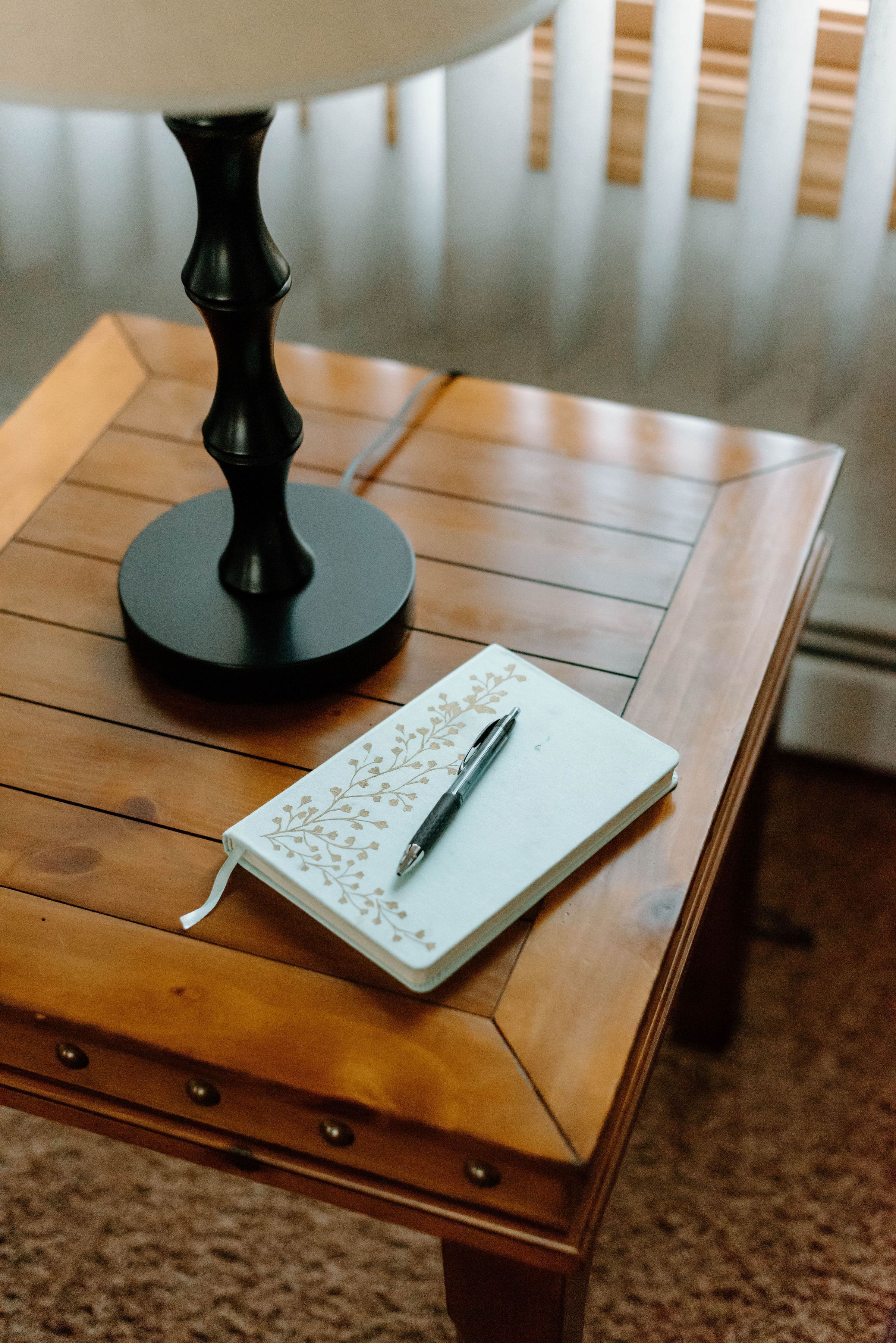 Una mesa de madera con una lámpara y un cuaderno con un bolígrafo encima.