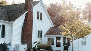 A white house with a brick chimney, a small porch, and a tree in the yard.