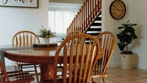 A dining area with a wooden table and chairs, a potted plant, a wall clock, and a staircase.