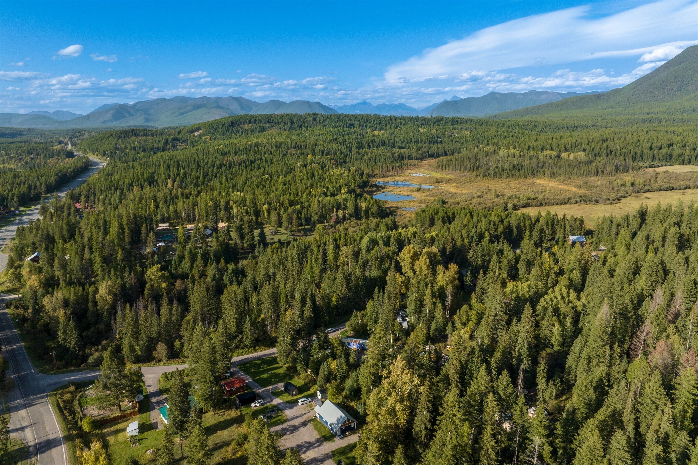 An aerial view of a forested area with a river, houses, and mountains in the background.
